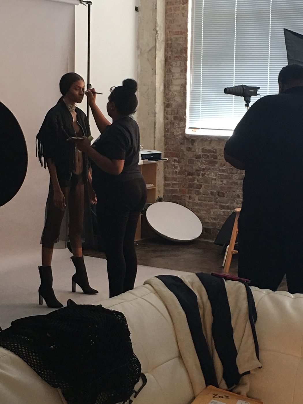 A makeup artist touches up the model's eye makeup between setups in a loft studio