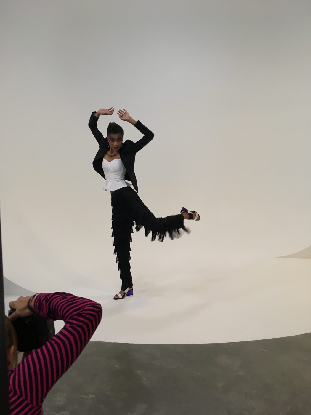 The model moves mid-pose on a white seamless backdrop to show how fringe trousers swing