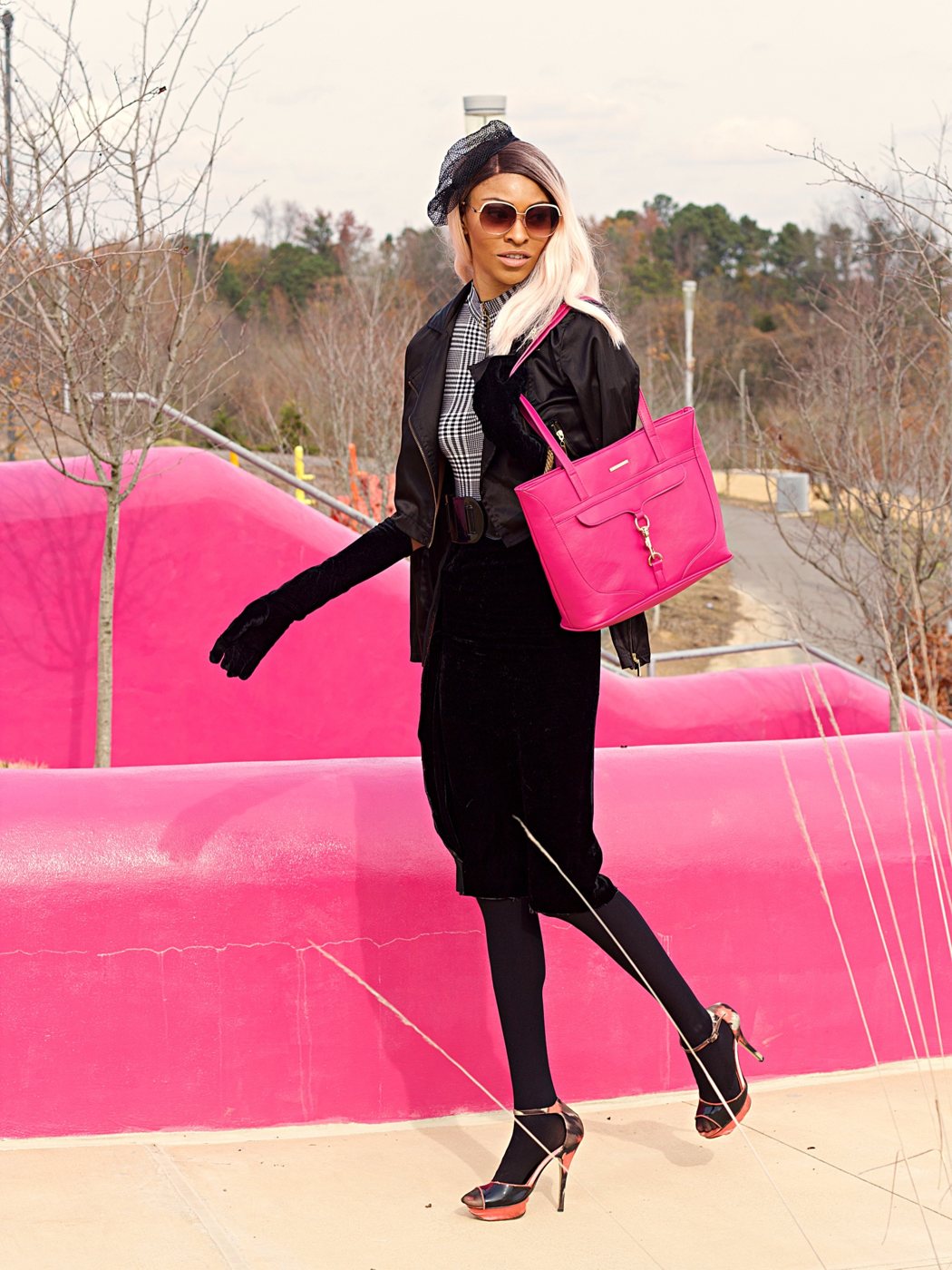Hot-pink tote carried past a pink sculptural wall with a black velvet look